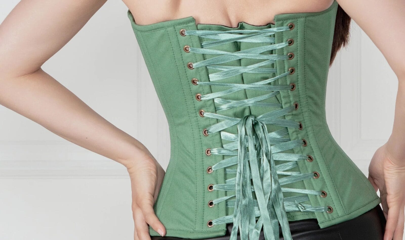Femme de dos en corset kaki à laçage traditionnel, pantalon simili cuir noir.