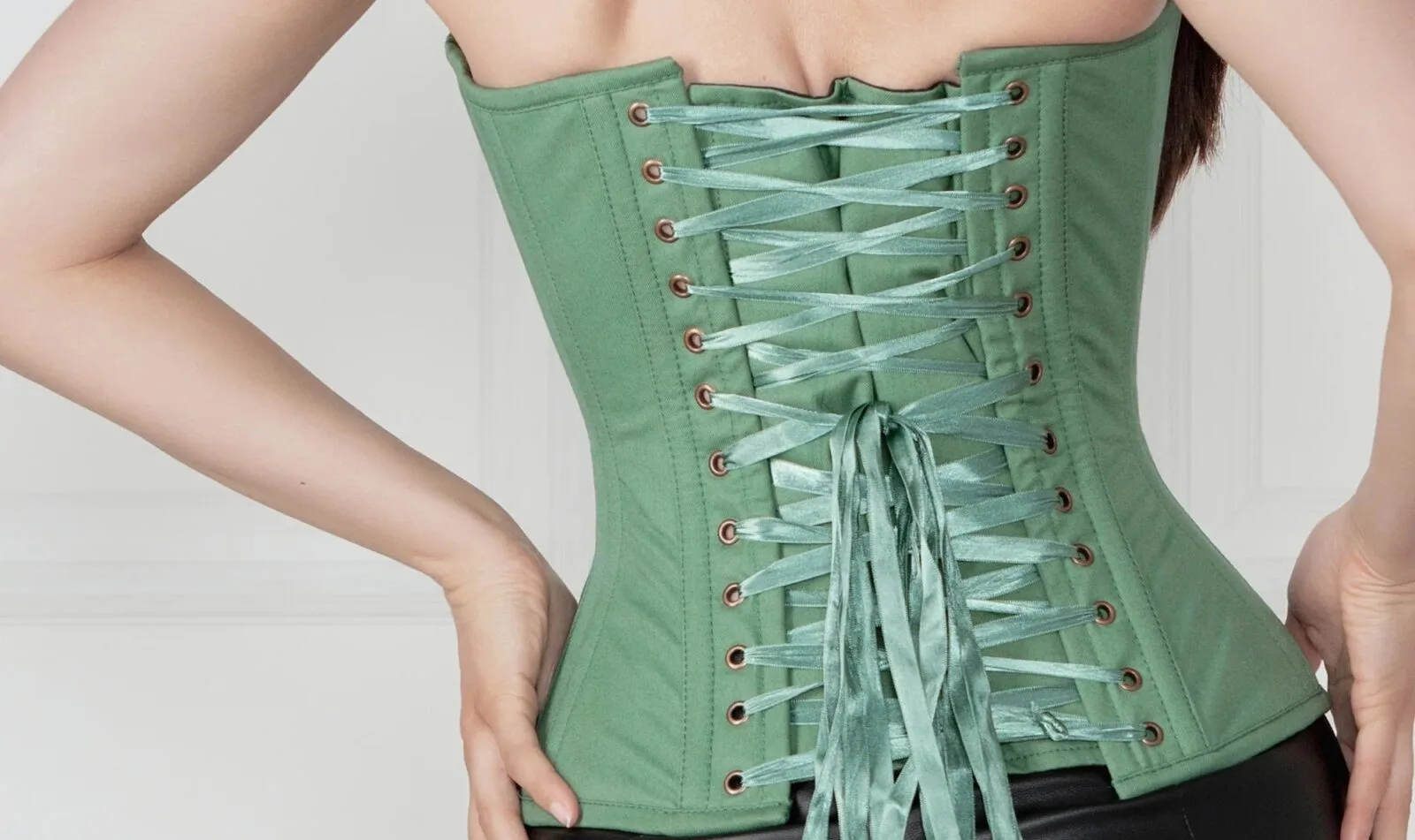 Femme de dos en corset kaki à laçage traditionnel, pantalon simili cuir noir.