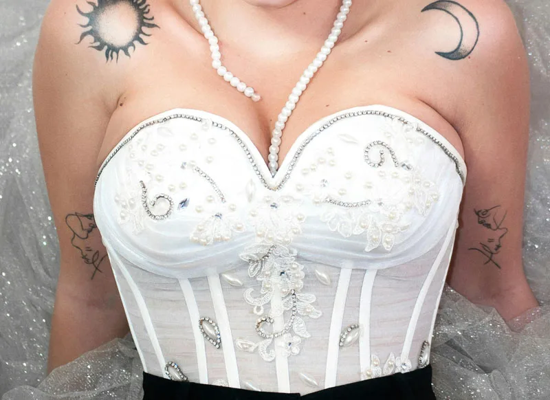 Zoom sur un bustier blanc à bonnets moulés et broderies argentées, porté avec un pantalon noir.